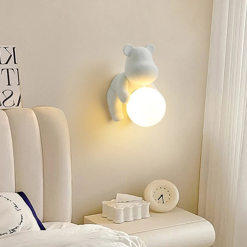 Nowoczesna lampa miś od SANDYHA w białym kolorze z okrągłym światłem zamontowana na ścianie przy łóżku