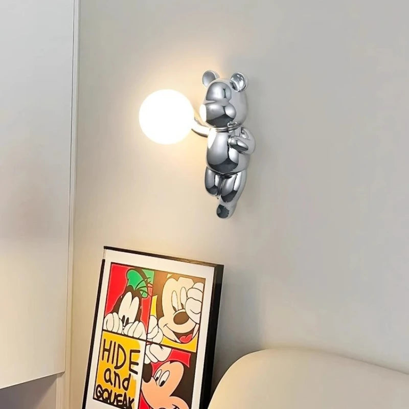 Lampa miś SANDYHA z chromowanym misiem trzymającym kulę świetlną na ścianie w nowoczesnym wnętrzu