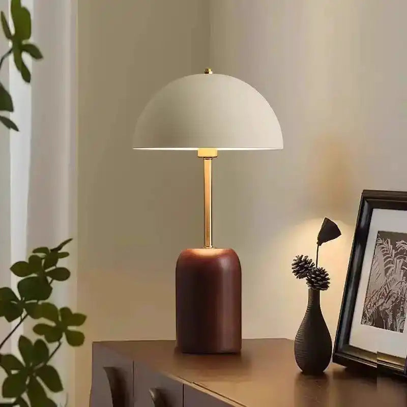 Elegancka lampa stołowa z białym półokrągłym kloszem i ciemną podstawą na drewnianym stoliku