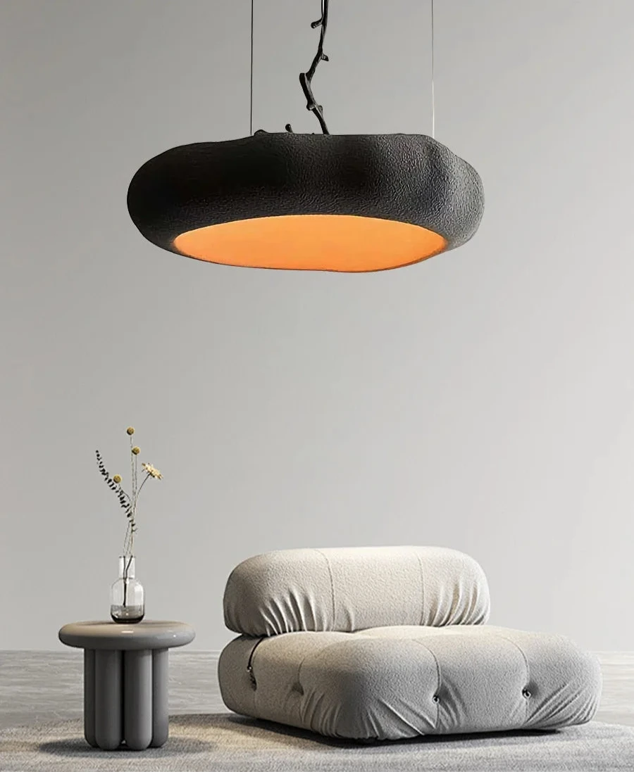 Czarna nowoczesna lampa wisząca Artpad nad jasnoszarym fotelem i stolikiem z wazonem