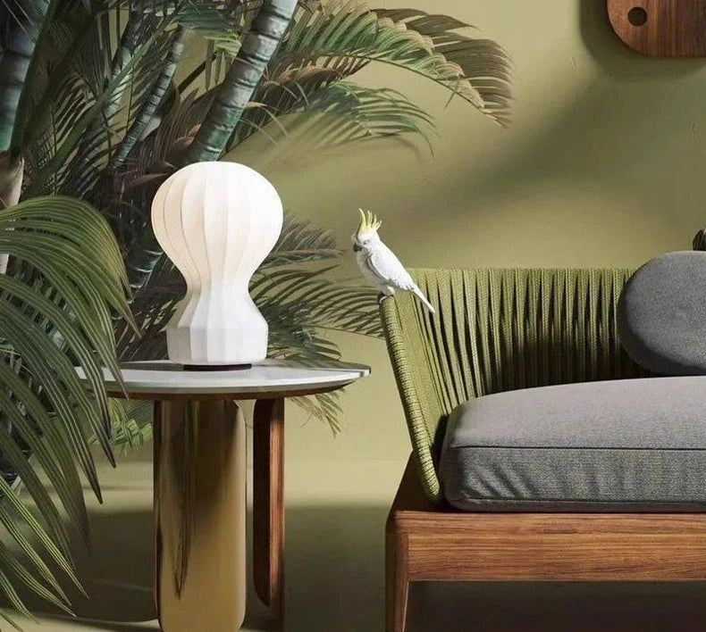 Designerska lampa barcato na stoliku obok zielonej sofy z ptakiem na oparciu