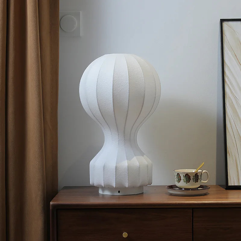 Designerska lampa barcato biała o nowoczesnym kształcie ustawiona na drewnianej komodzie
