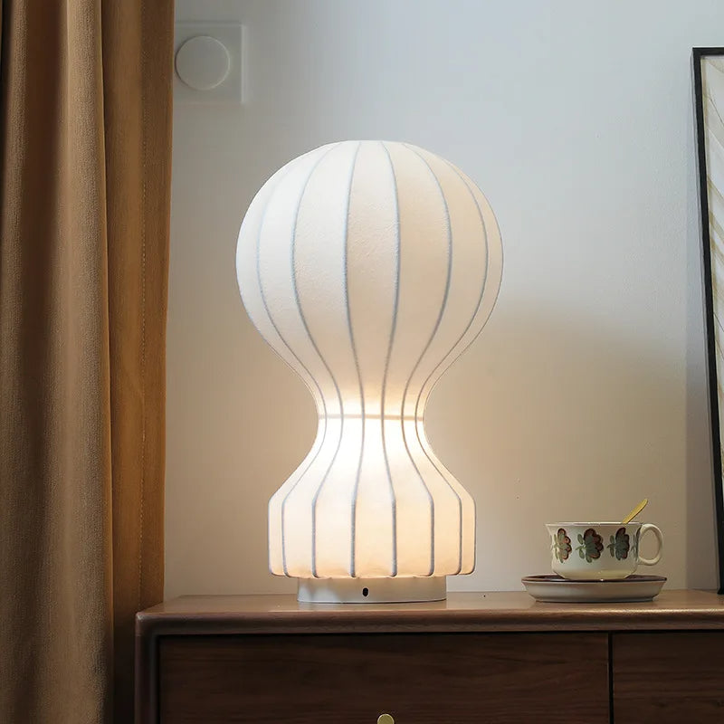 Designerska lampa Barcato w nowoczesnym kształcie na drewnianej komodzie obok filiżanki