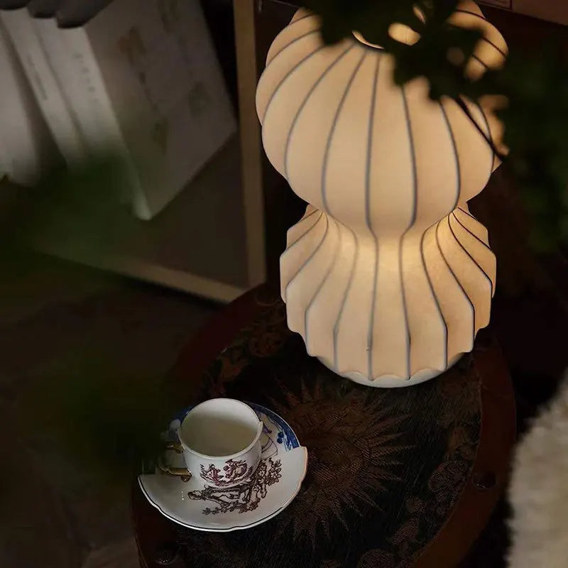 Designerska lampa barcato emitująca ciepłe światło obok filiżanki na ciemnym stoliku