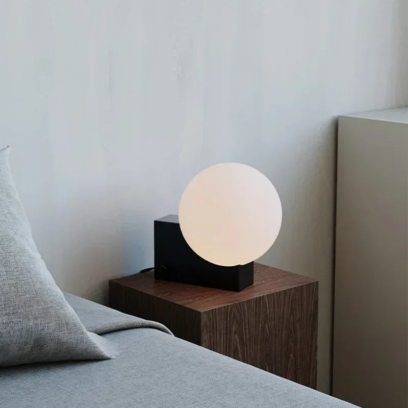 Nowoczesna lampa biurkowa JIANKEXING z białą kulistą lampą na czarnej podstawie na drewnianym stoliku