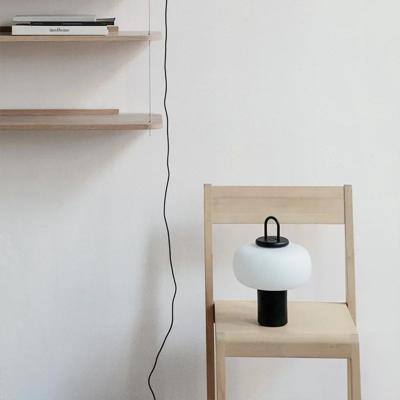 Lampa biurkowa SANDYHA w nowoczesnym stylu na drewnianym krześle w jasnym pomieszczeniu