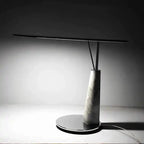 Nowoczesna lampa biurkowa z marmurową podstawą i cienkim czarnym ramieniem do oświetlenia stanowiska pracy