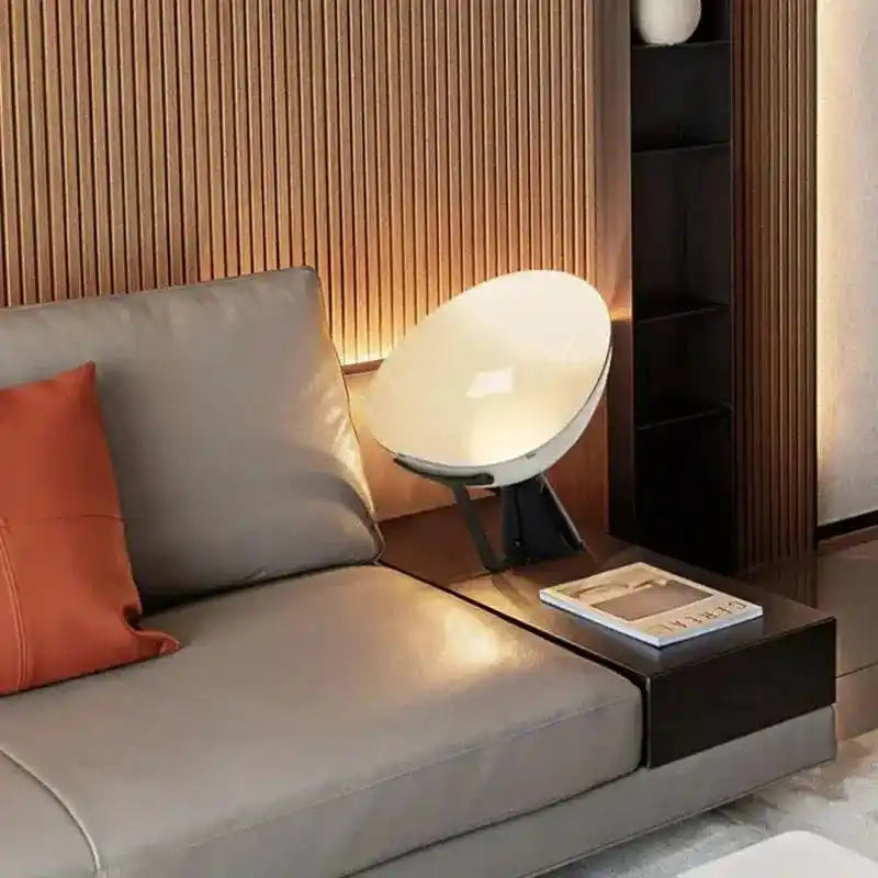 Lampa biurkowa JIANKEXING o nowoczesnym designie obok szarej sofy z pomarańczową poduszką