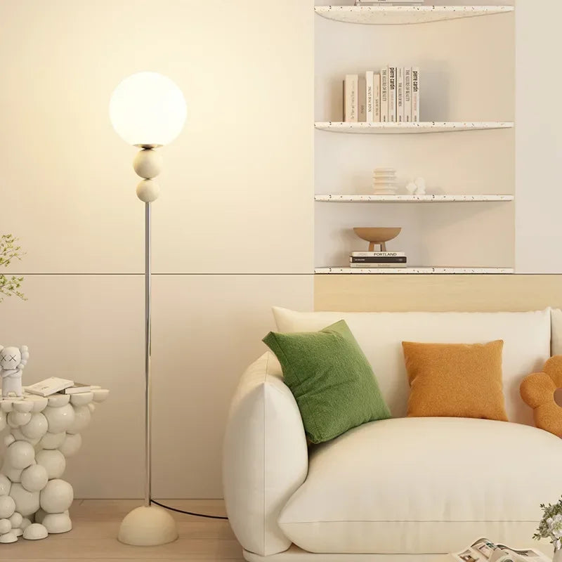 Lampa podłogowa SANDYHA z kulistym kloszem w nowoczesnym salonie z białą sofą i kolorowymi poduszkami