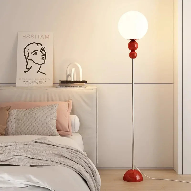 Lampa podłogowa SANDYHA z białą kulistą kloszem i czerwonymi akcentami stojąca obok łóżka w nowoczesnej sypialni