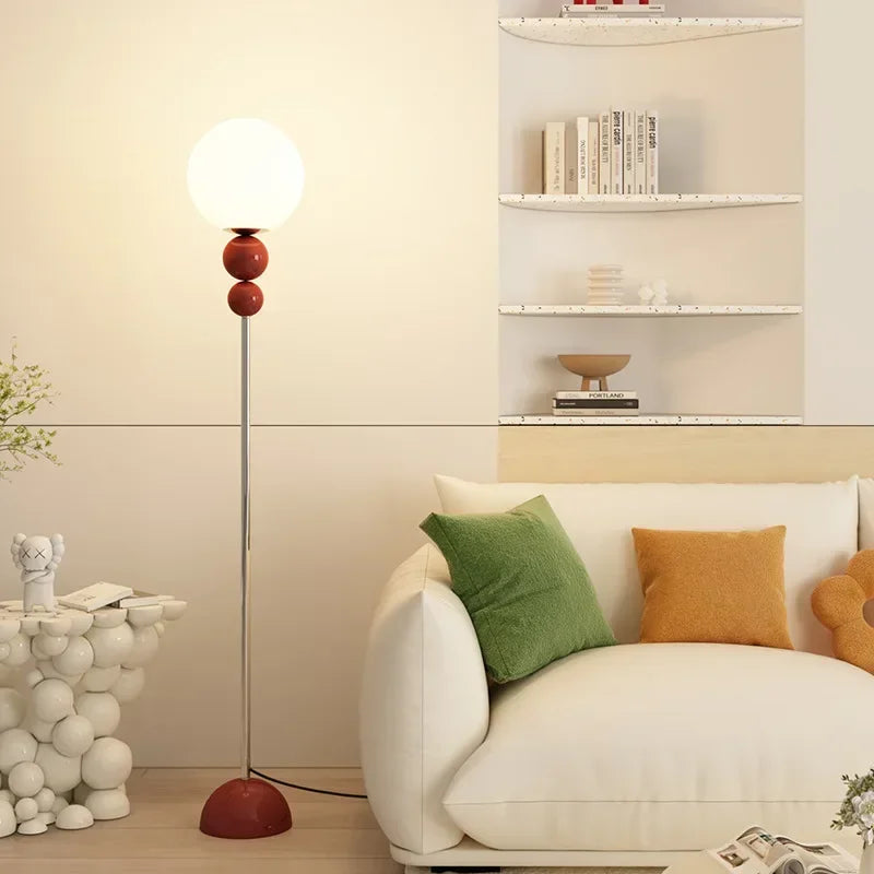 Lampa podłogowa SANDYHA z kulistym kloszem i czerwonymi detalami stojąca obok kanapy w salonie