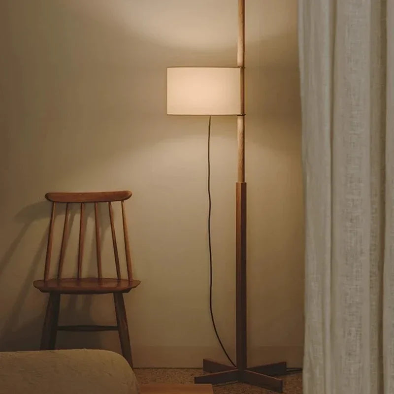 Nowoczesna lampa podłogowa z beżowym abażurem obok drewnianego krzesła w przytulnym wnętrzu