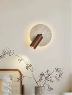 Nowoczesna lampa ścienna z metalowym cylindrem i okrągłą podstawą montowana na jasnej ścianie w salonie