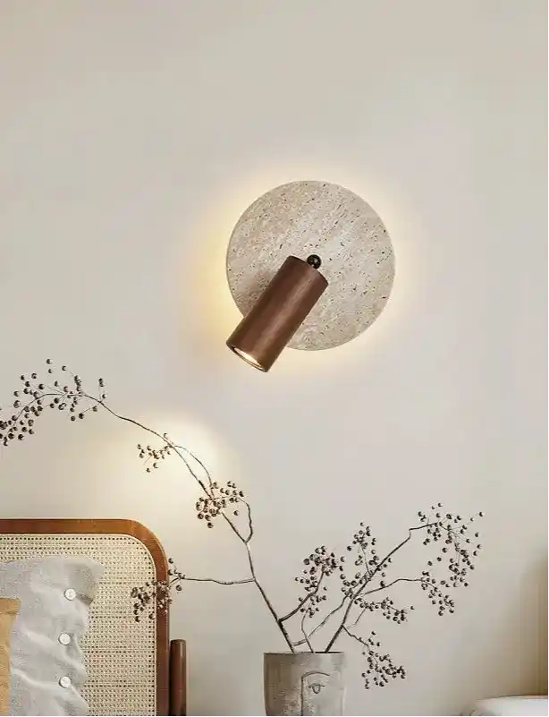 Nowoczesna lampa ścienna z metalowym cylindrem i okrągłą podstawą montowana na jasnej ścianie w salonie