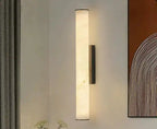 Nowoczesna lampa ścienna w kształcie smukłego walca emitująca ciepłe światło na szarej ścianie