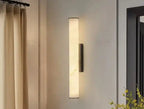Nowoczesna lampa ścienna w kształcie pionowego walca zamontowana na jasnej ścianie w salonie