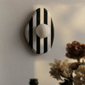 Nowoczesna lampa ścienna IWP w czarno-białe paski z okrągłym kloszem na jasnej ścianie