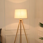 Elegancka lampa stojąca do salonu z jasnym abażurem i drewnianą podstawą na trójnogu