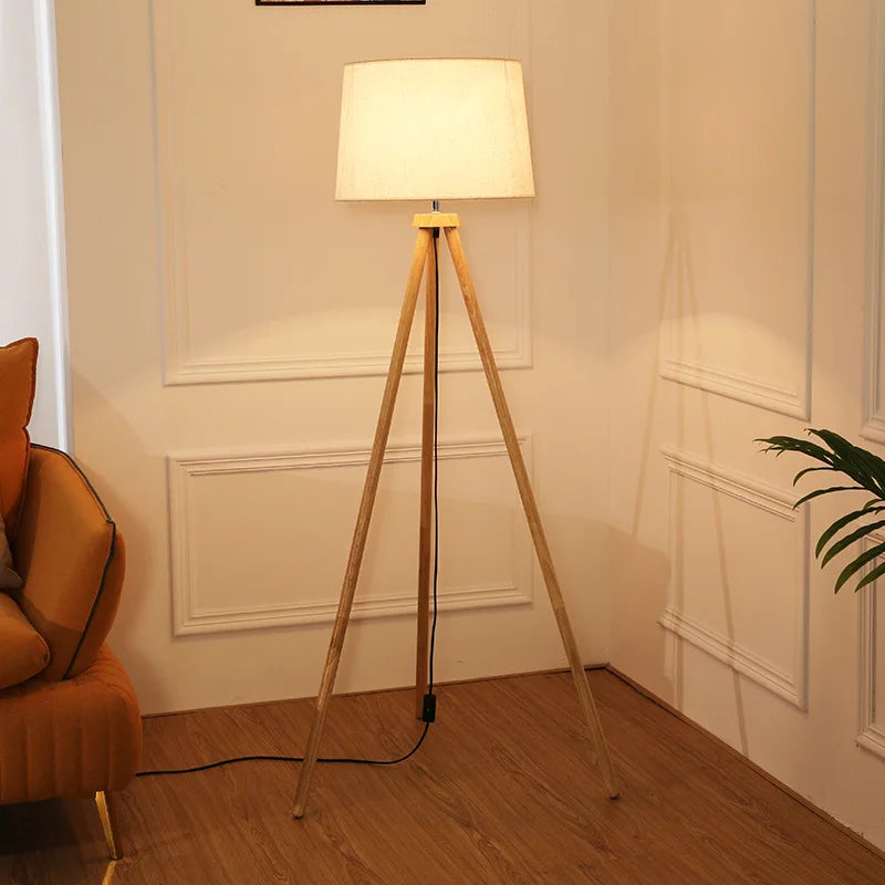 Lampa stojąca do salonu z drewnianą podstawą i białym abażurem na trójnogu