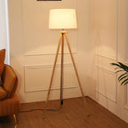 Lampa stojąca do salonu z drewnianą podstawą i białym abażurem na trójnogu