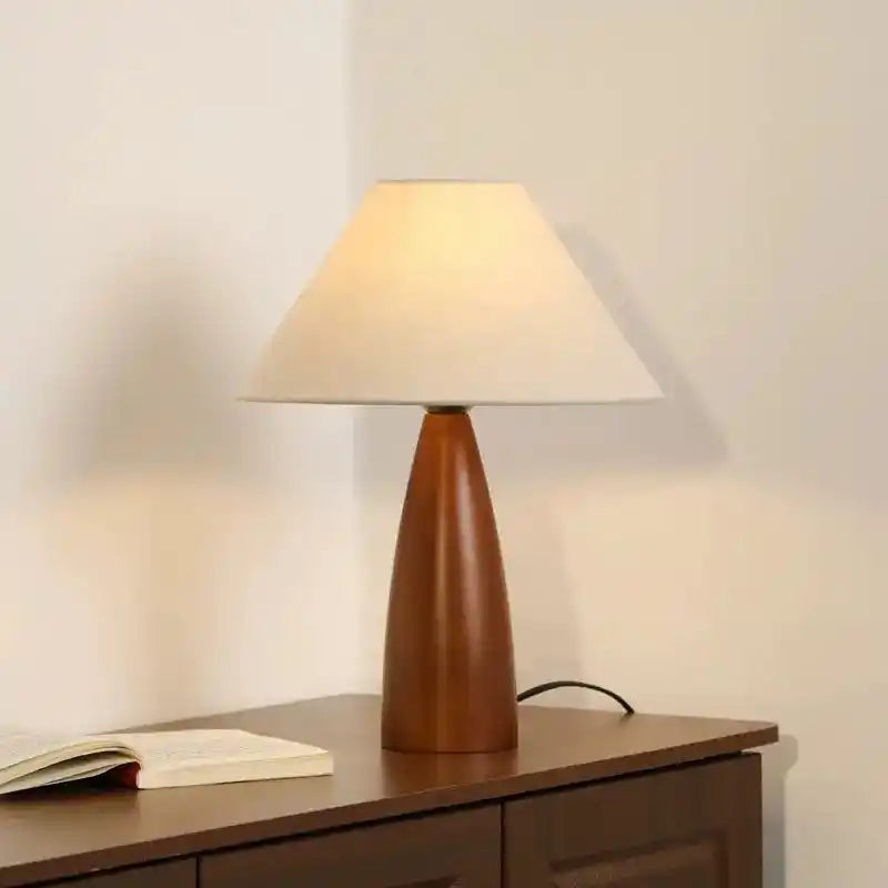 Lampa stołowa z drewnianą podstawą i kremowym abażurem na ciemnym meblu marki Inny dom