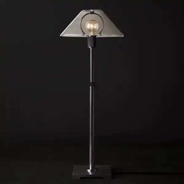 Czarna lampa stołowa z przezroczystym kloszem i widoczną żarówką na ciemnym tle