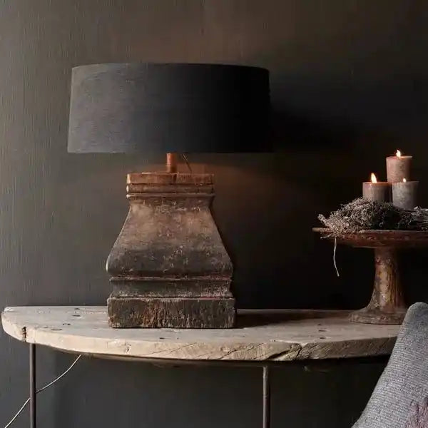 Lampa stołowa z czarnym abażurem i rustykalną podstawą na drewnianym stole przy ciemnej ścianie