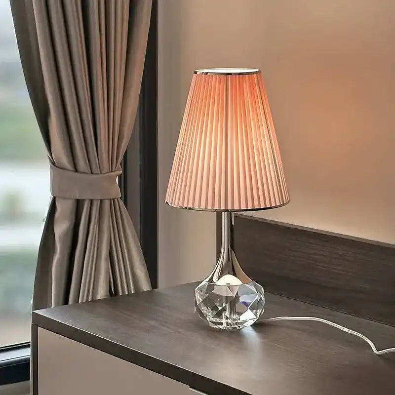 Elegancka lampa stołowa Moss z plisowanym abażurem i kryształową podstawą na ciemnym stoliku