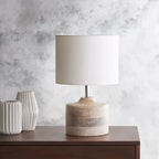 Lampa stołowa z białym cylindrycznym abażurem i drewnianą podstawą na szafce