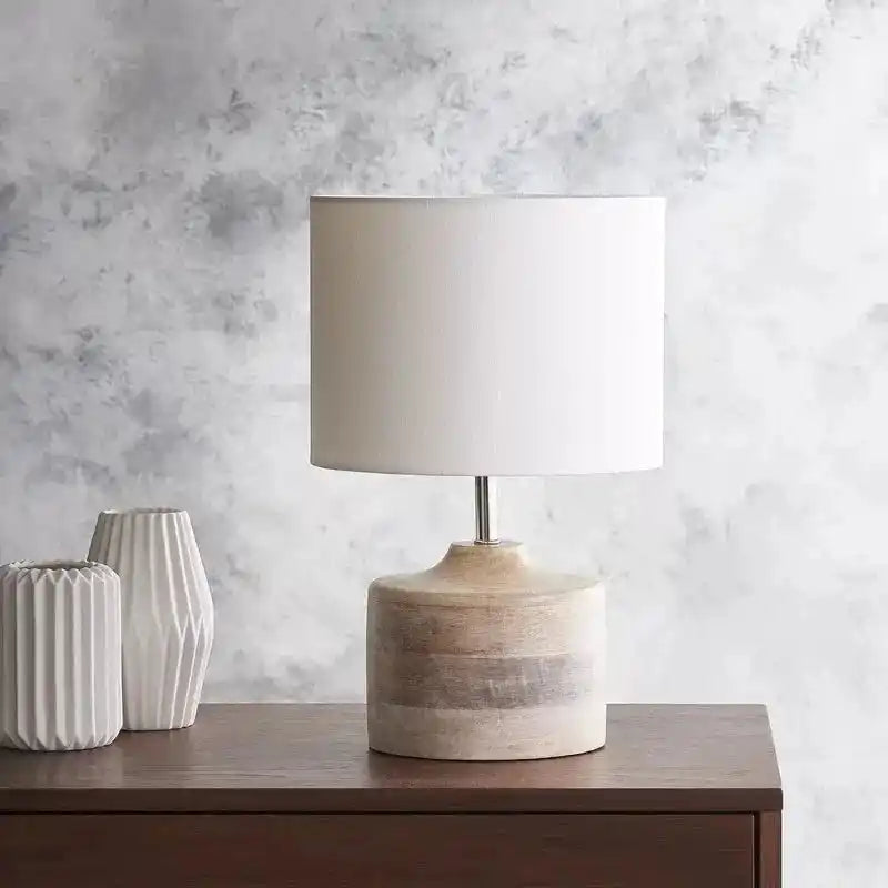Lampa stołowa z białym cylindrycznym abażurem i drewnianą podstawą na szafce