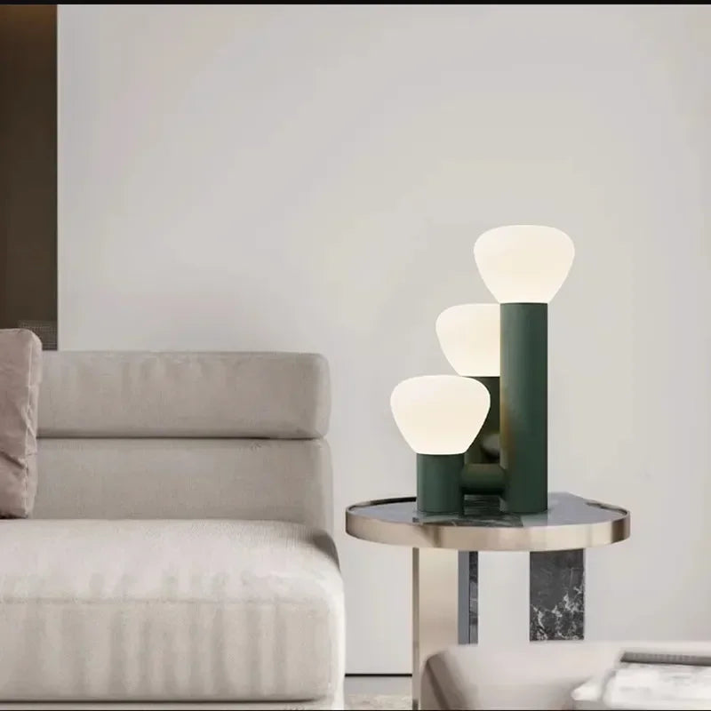 Nowoczesna lampa stołowa JIANKEXING z trzema szklanymi kloszami i zieloną podstawą na stoliku obok kanapy