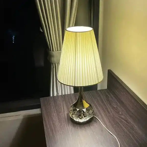 Lampa stołowa Moss z eleganckim plisowanym abażurem i kryształową podstawą na ciemnym drewnianym biurku
