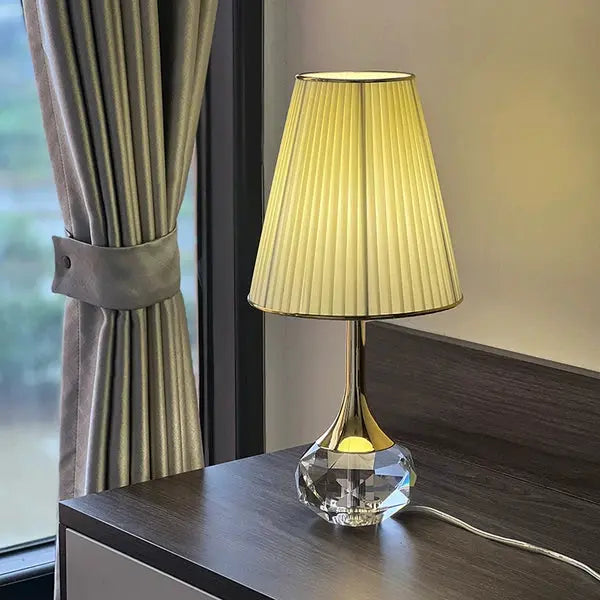 Lampa stołowa Moss z plisowanym abażurem i kryształową podstawą na ciemnym stole