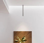 Minimalistyczna czarna lampa sufitowa wisząca nad obrazem z liśćmi na białej ścianie