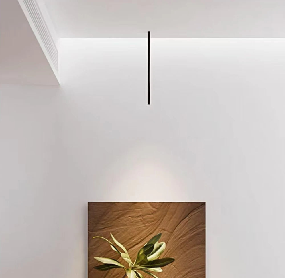 Minimalistyczna czarna lampa sufitowa wisząca nad obrazem z liśćmi na białej ścianie