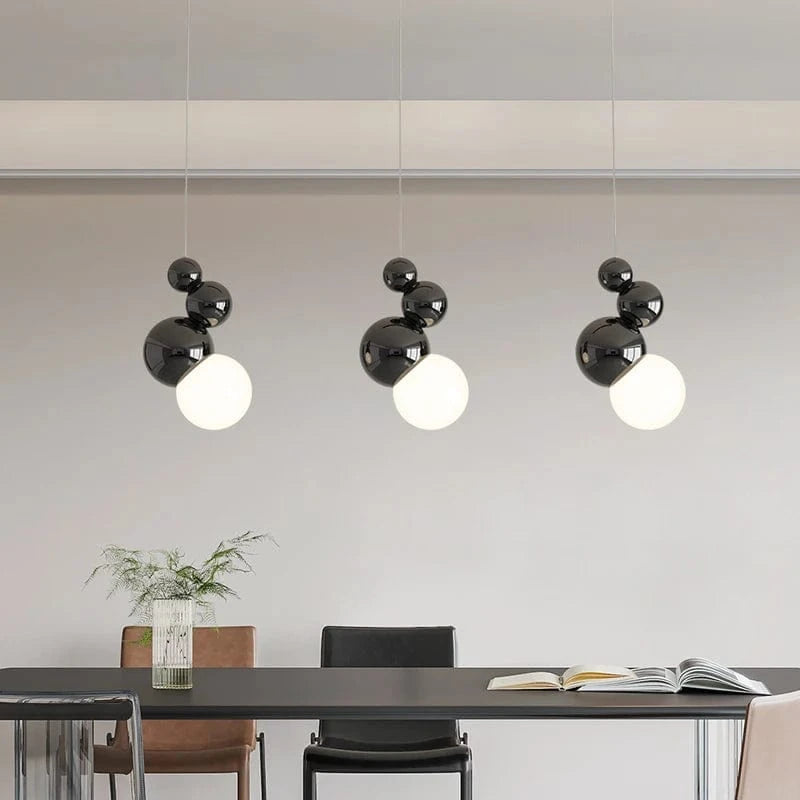 Lampa wisząca z trzema czarnymi abażurami i białymi kuleczkami nad stołem w jadalni