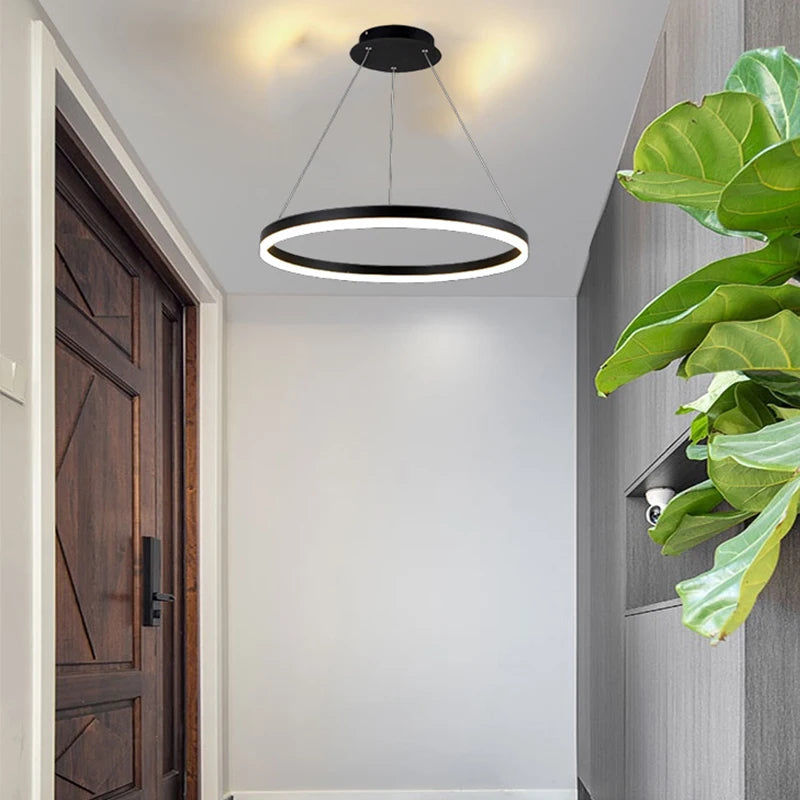 Nowoczesna czarna lampa wisząca w formie podświetlanego okręgu na białym suficie w przedpokoju